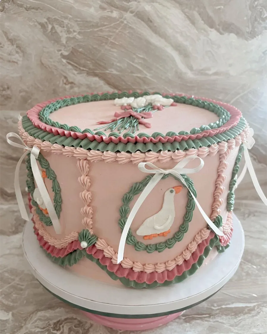 Tall pink custom cake with green garlands, white bows and piped dove wreaths